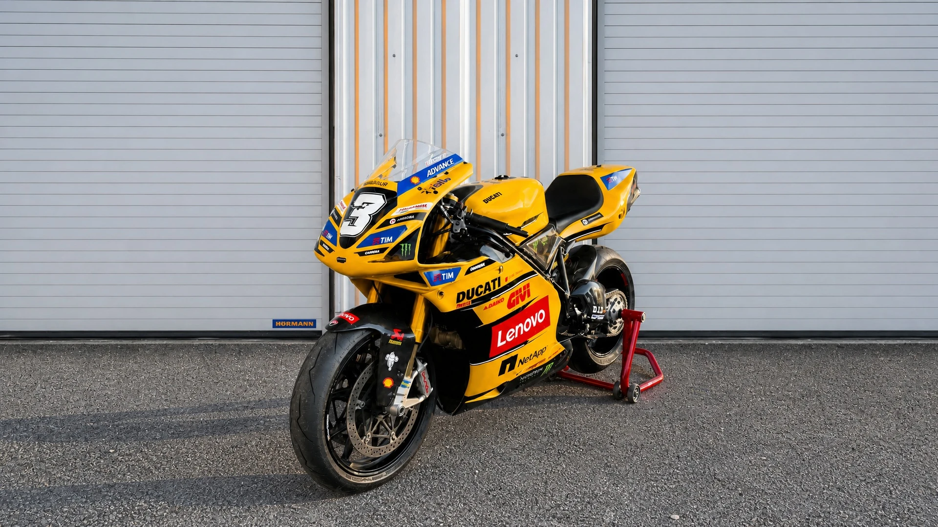 Moto de course Ducati MotoGP jaune vif stationnée devant des portes de garage industrielles Hörmann