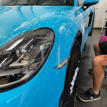Technicien en atelier applique à la main un film PPF (Paint Protection Film) transparent sur le capot d'une Porsche 911 jaune Racing