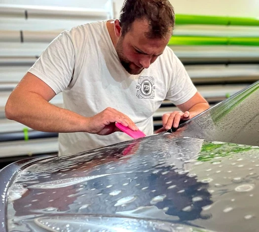 Technicien appliquant un film de protection PPF (Paint Protection Film) sur le pare-brise d'une Alpine jaune vif, en atelier de pose