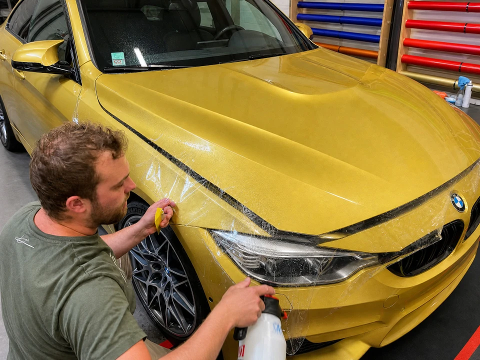 Carrosserie bleue d'un véhicule Alpine A110 «Turini», partiellement recouverte de ruban de masquage papier crêpé jaune, disposé en couches superposées formant un gabarit de découpe
